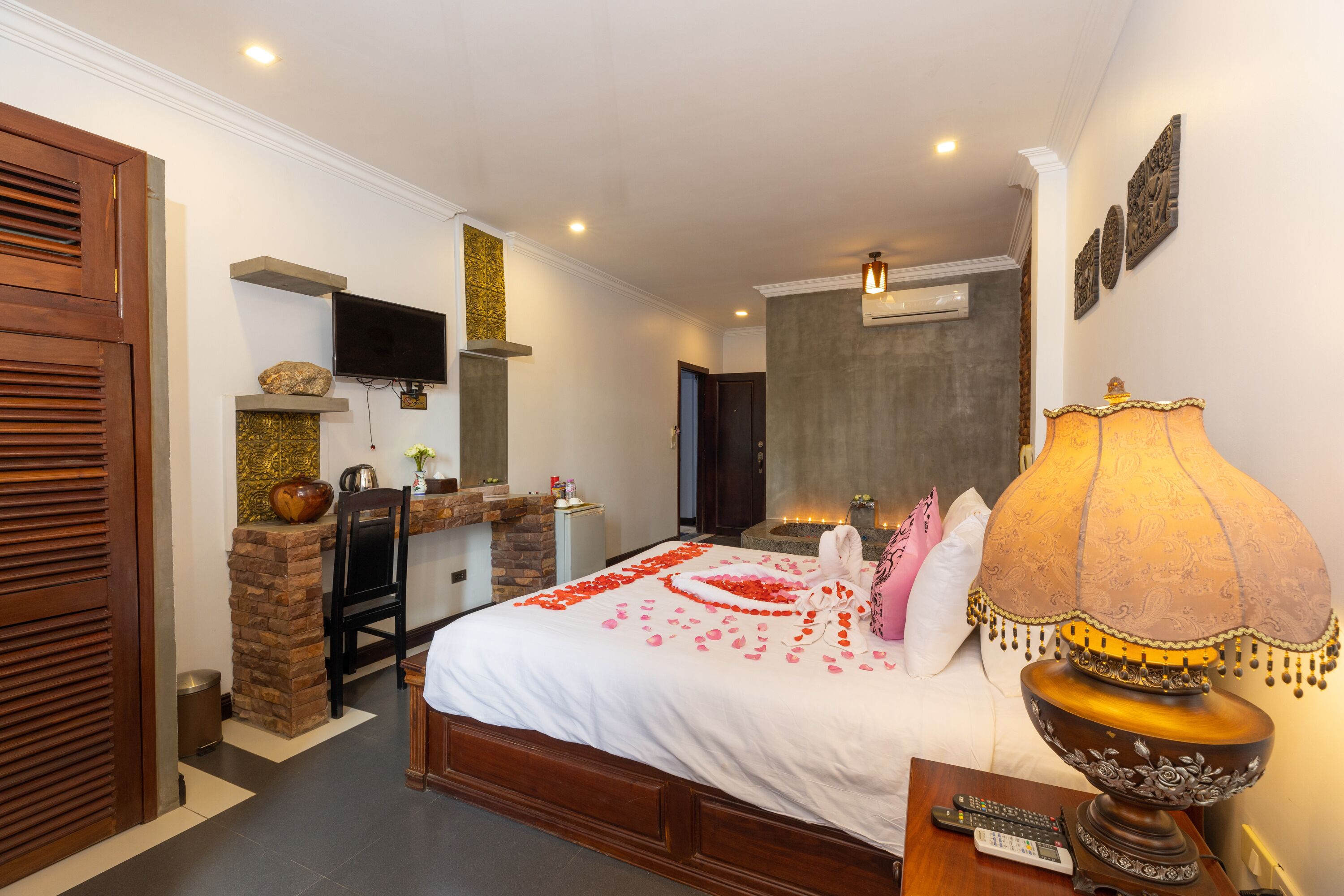 A hotel room with a bed, a TV, a stone fireplace, a lamp, and a wooden door.