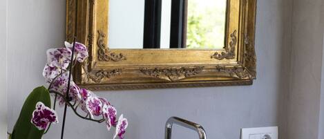 A bathroom with a white sink, a gold-framed mirror, a potted orchid, and two black cups.