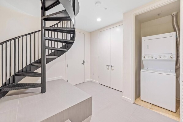 A modern apartment with a spiral staircase, white wardrobes, and a built-in washer and dryer.
