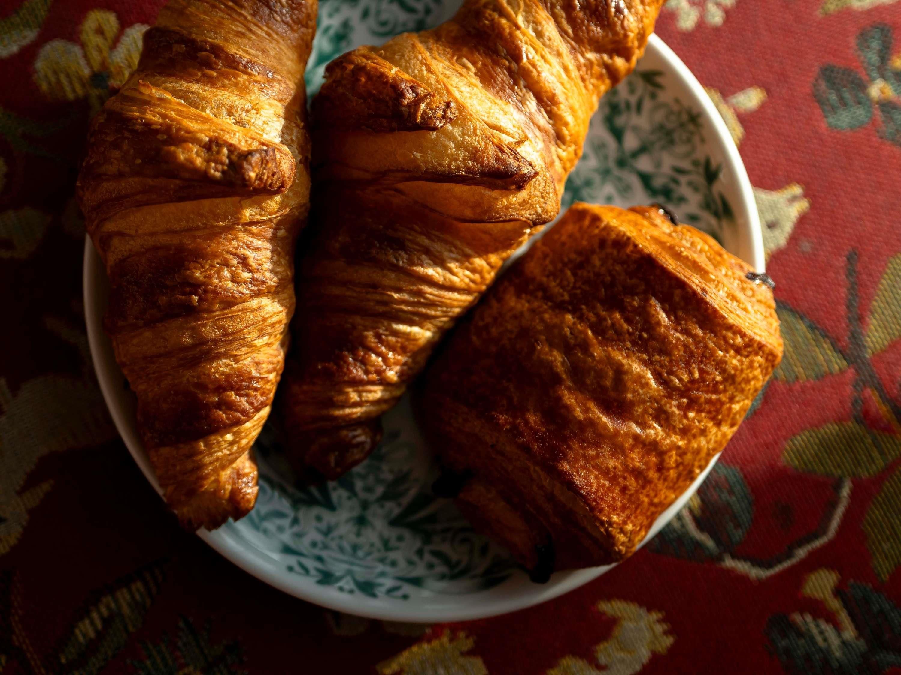 A plate with three croissants on a patterned tablecloth.