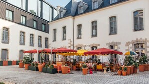A courtyard with outdoor seating, potted plants, and a building with large windows and a tiled roof. - Mama Shelter Rennes (Rennes)