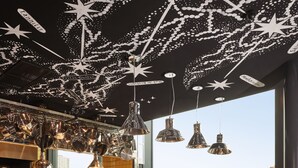 A restaurant with a high ceiling decorated with stars, a view of the city, and a traditional wooden table with chairs. - Mama Shelter Rennes (Rennes)