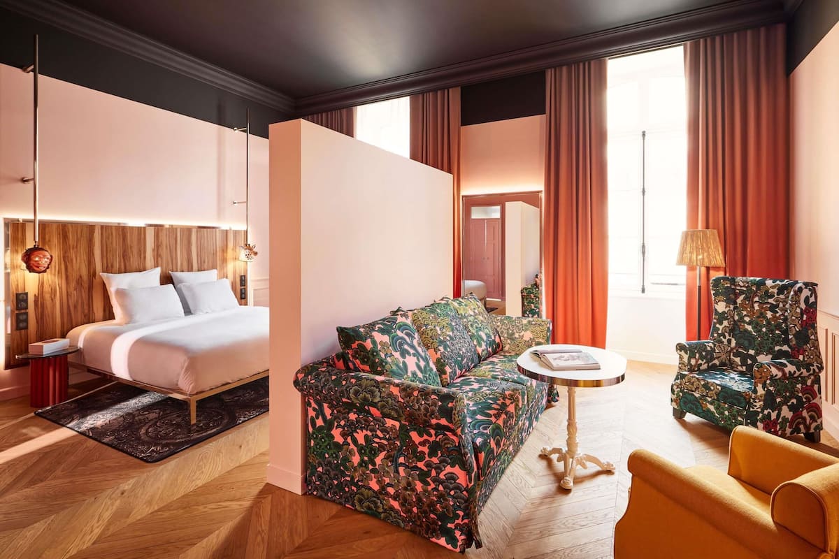 A hotel room with a bed, a sofa, a chair, and a small table.