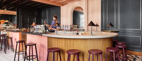 Zona de bar con un bartender, taburetes y una barra.