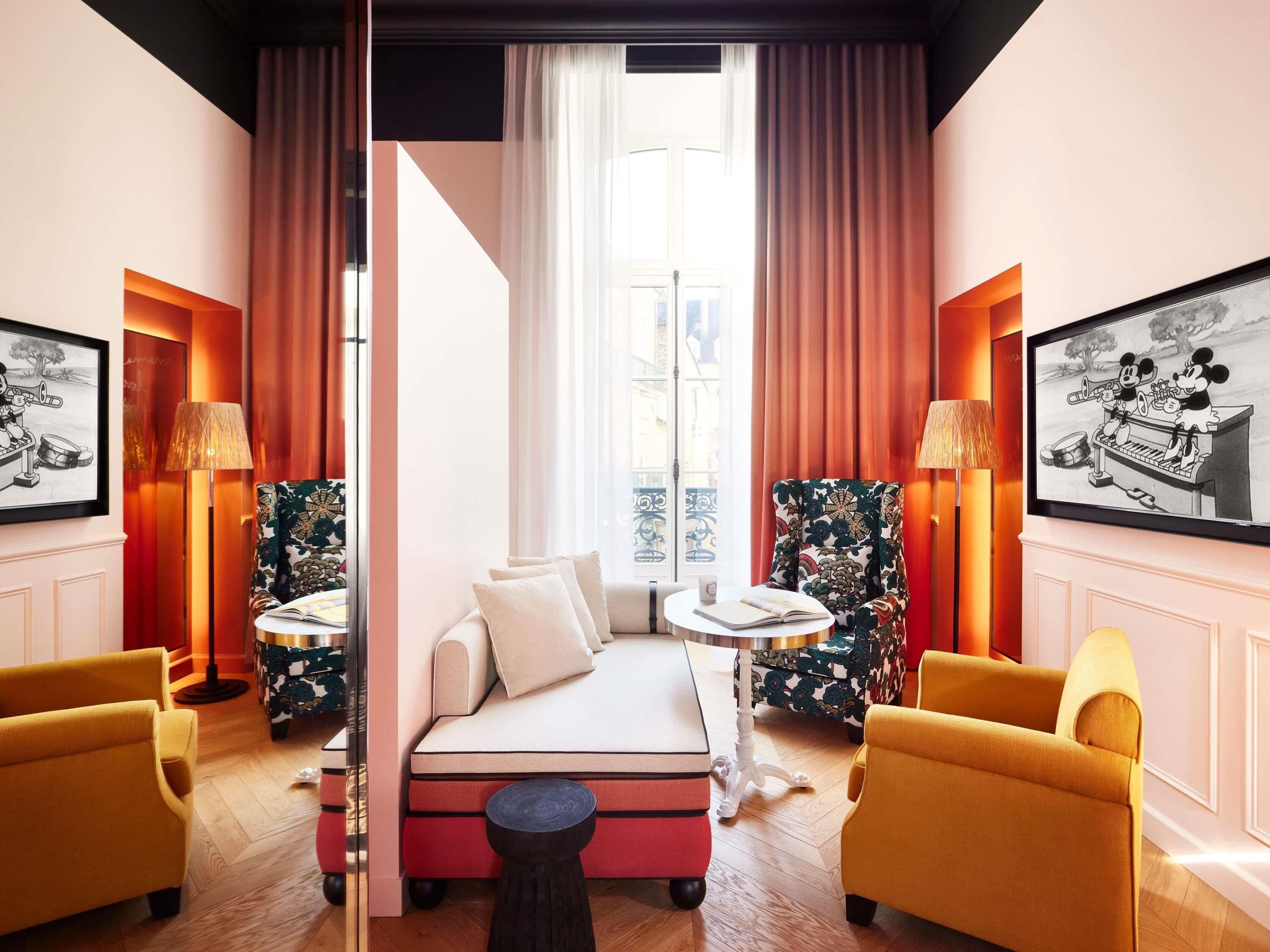 A hotel room with a bed, two armchairs, a small round table, a side table, and a television.