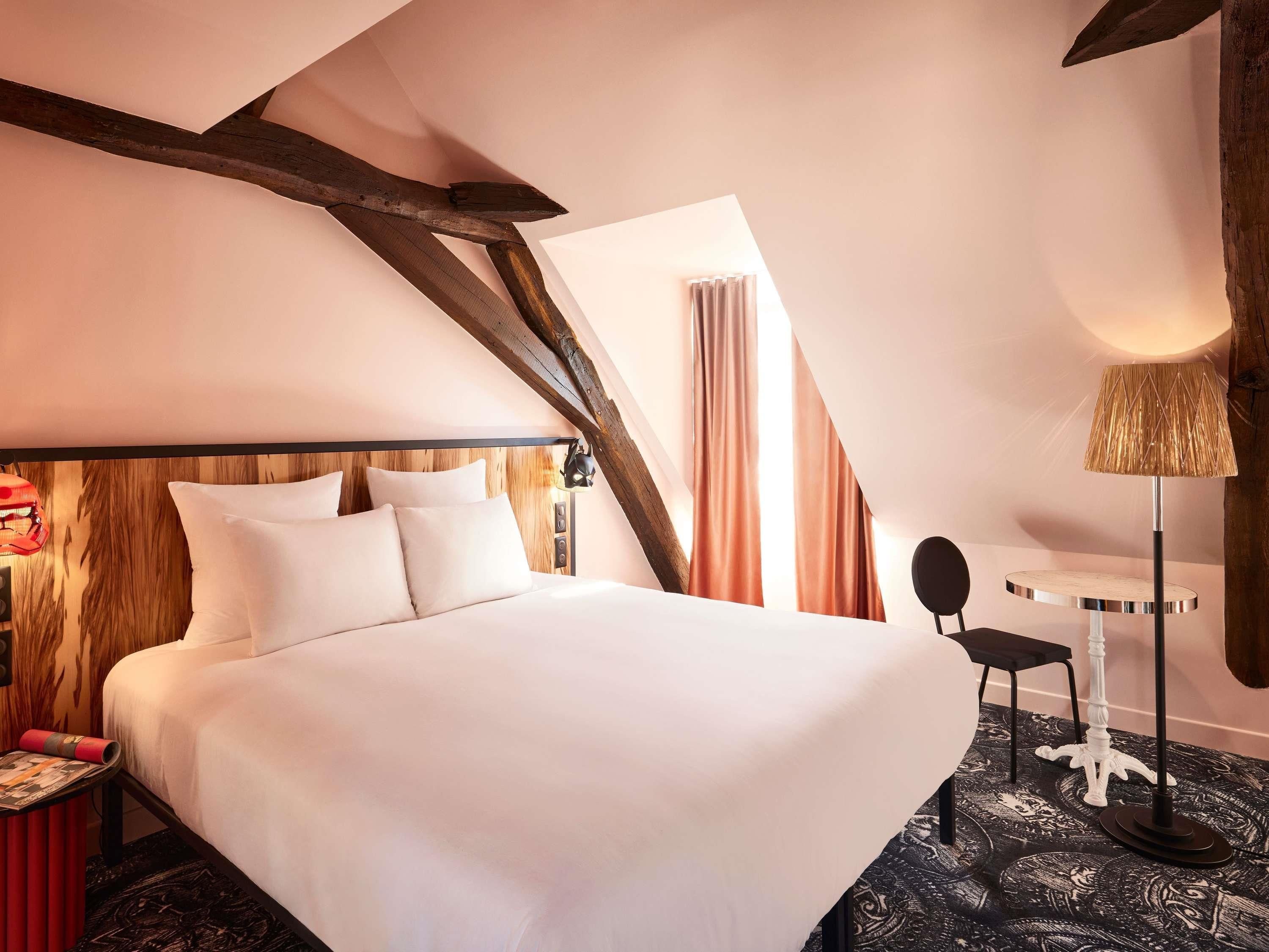 A hotel room with a large bed, a desk, a lamp, and a window with curtains.