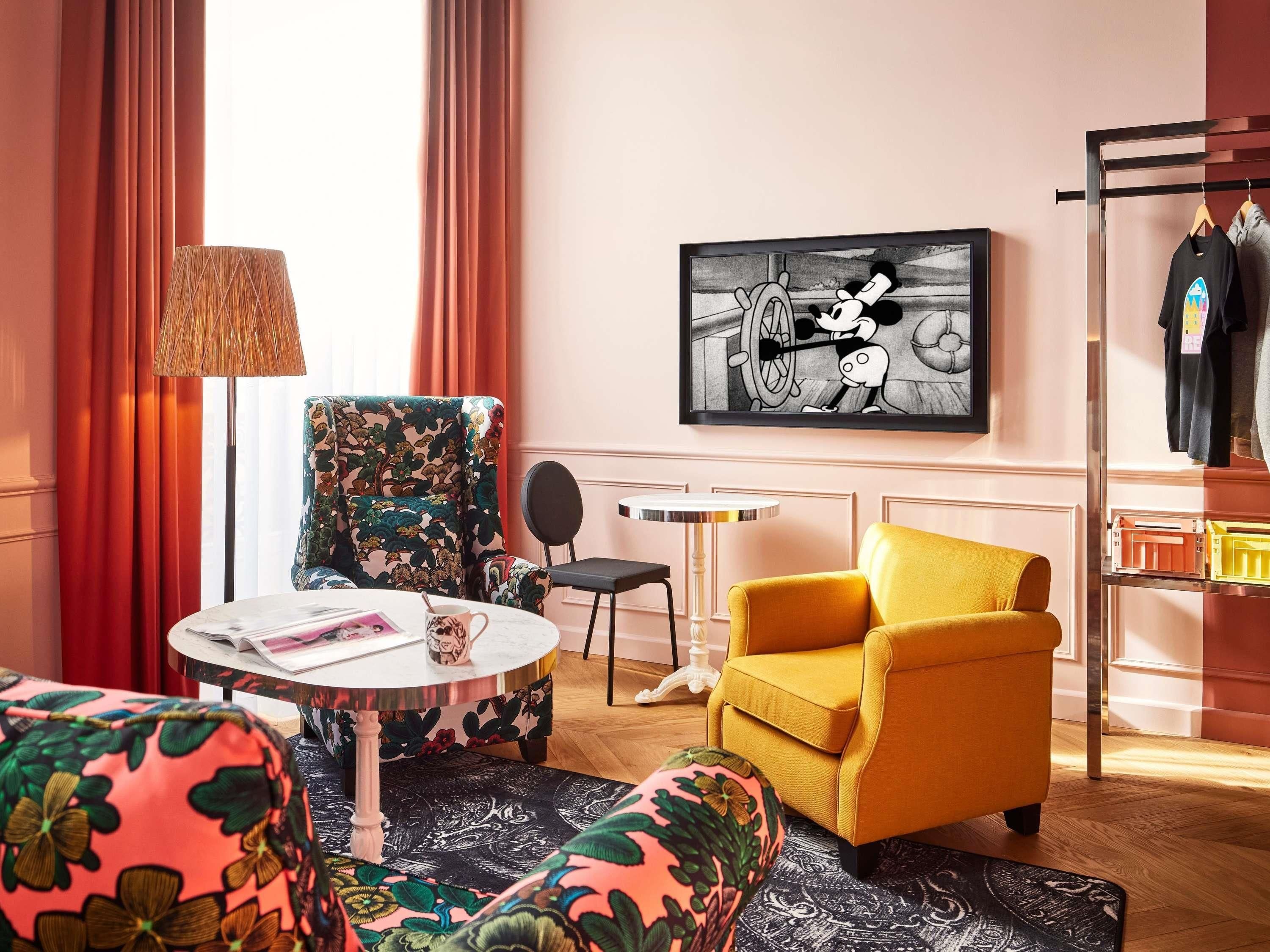 A hotel room with a sofa, armchair, round table, and a painting on the wall.