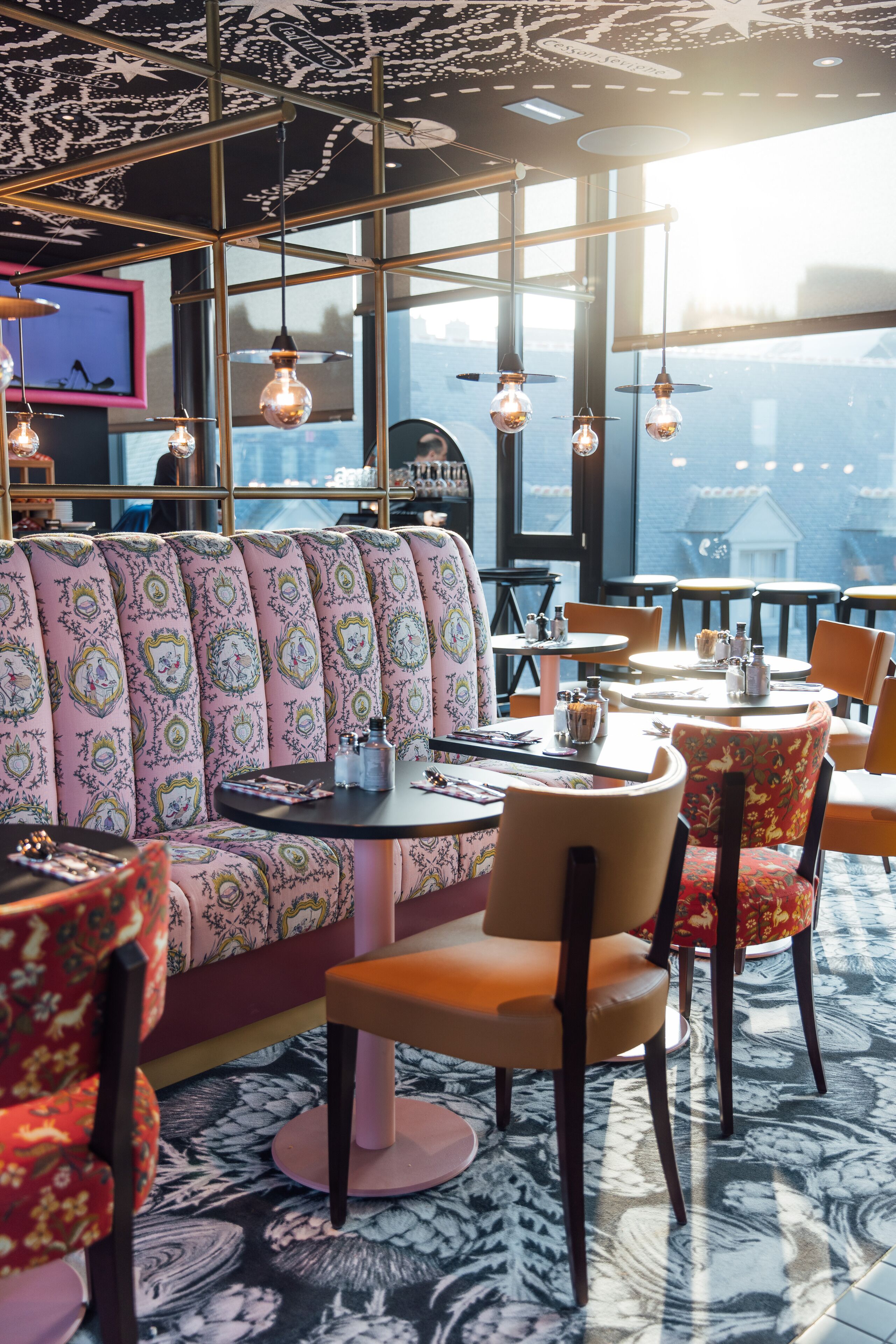 Un restaurant chaleureux avec des sièges à motifs, des tables rondes et des luminaires suspendus.