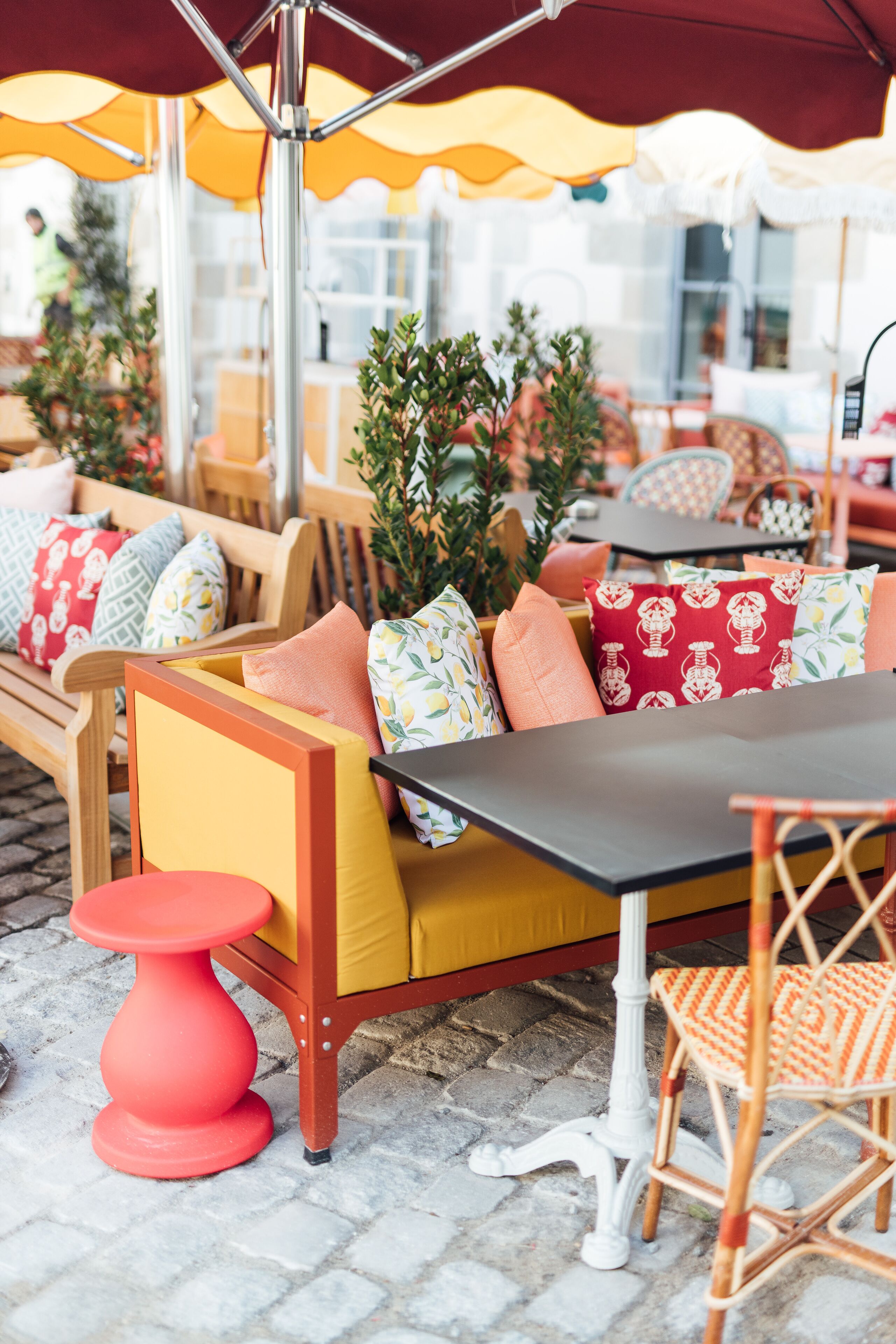 Un espace extérieur aménagé avec des meubles en bois, des coussins jaunes et des oreillers à motifs rouges et blancs.
