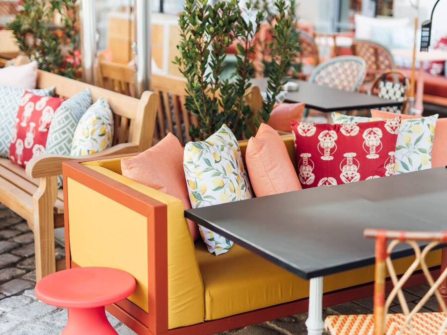 An outdoor seating area with wooden furniture, yellow cushions, and red and white patterned pillows.