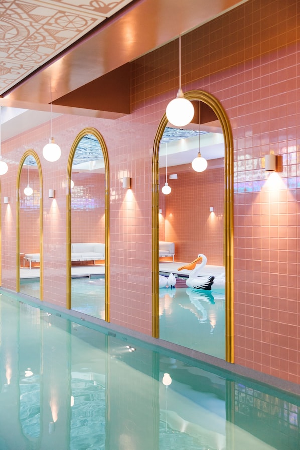 Un área de piscina interior moderna con espejos arqueados y una escultura de cisne.