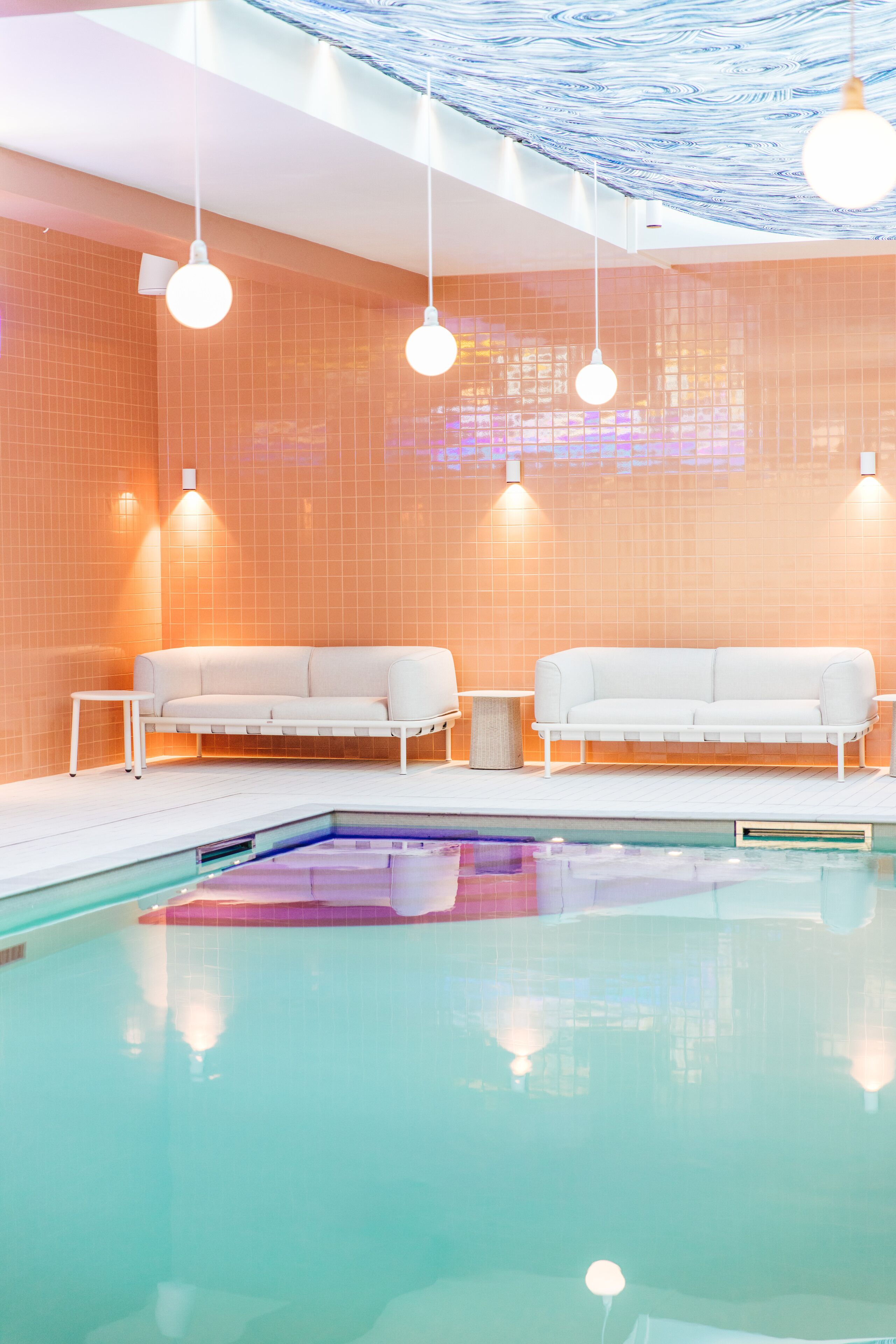 Un'area piscina interna moderna con due divani bianchi e lampade a sospensione.