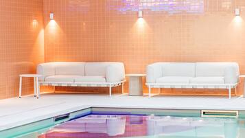 Un'area piscina interna moderna con due divani bianchi e lampade a sospensione.