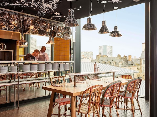 A restaurant with a high ceiling, hanging pots, and a city view.
