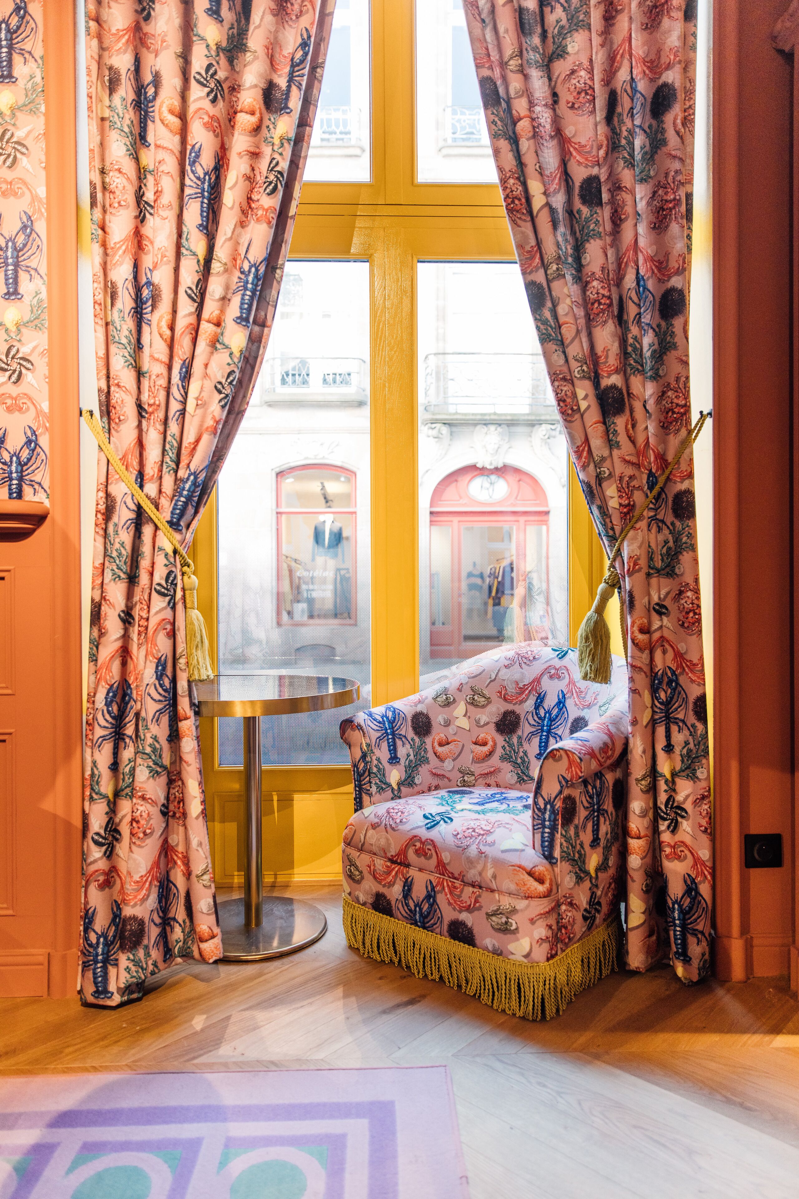 Une pièce avec un fauteuil à motifs, une table ronde et des rideaux ornés de motifs floraux.