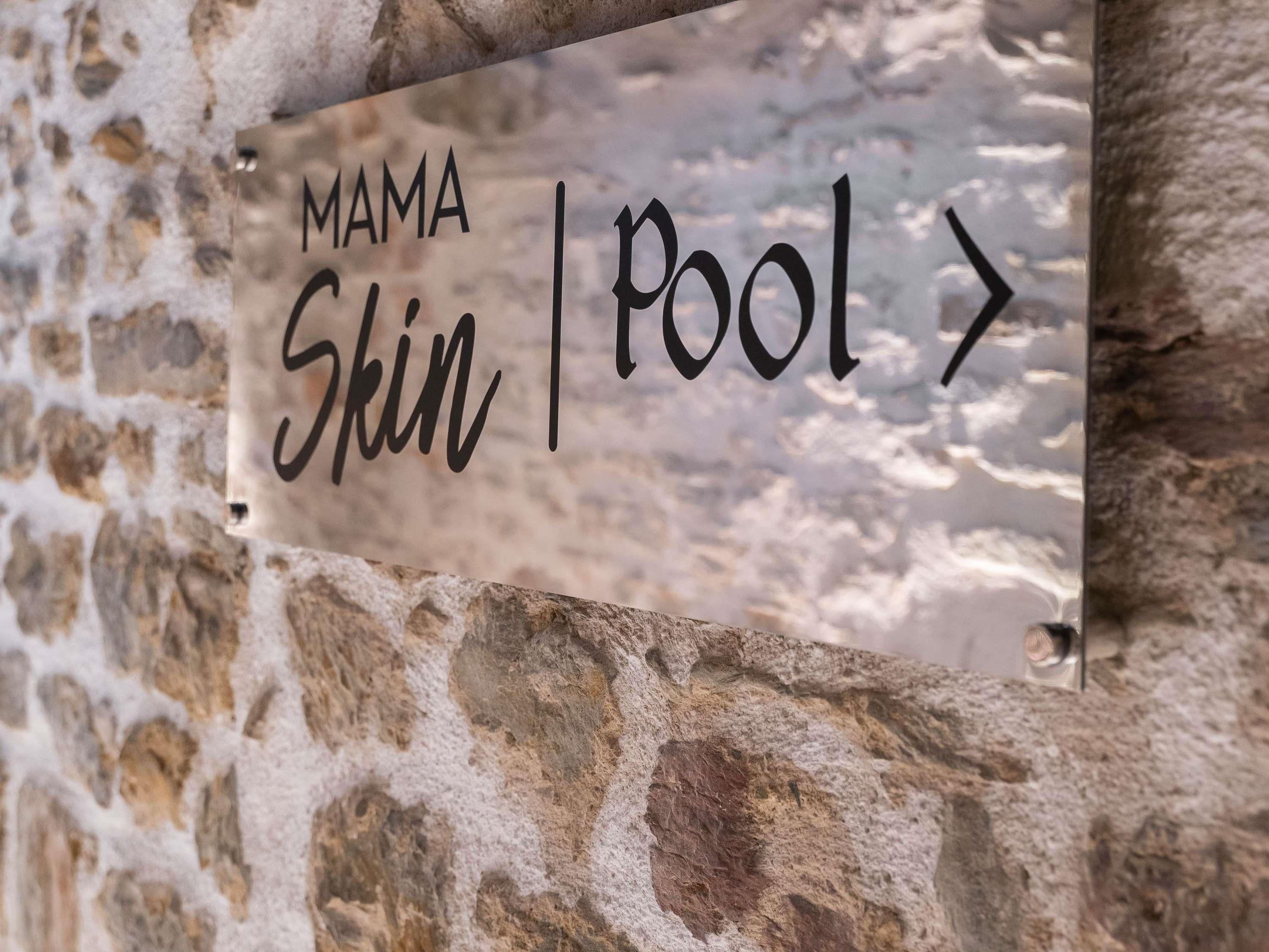 A sign with the text 'MAMA Skin Pool' mounted on a stone wall.