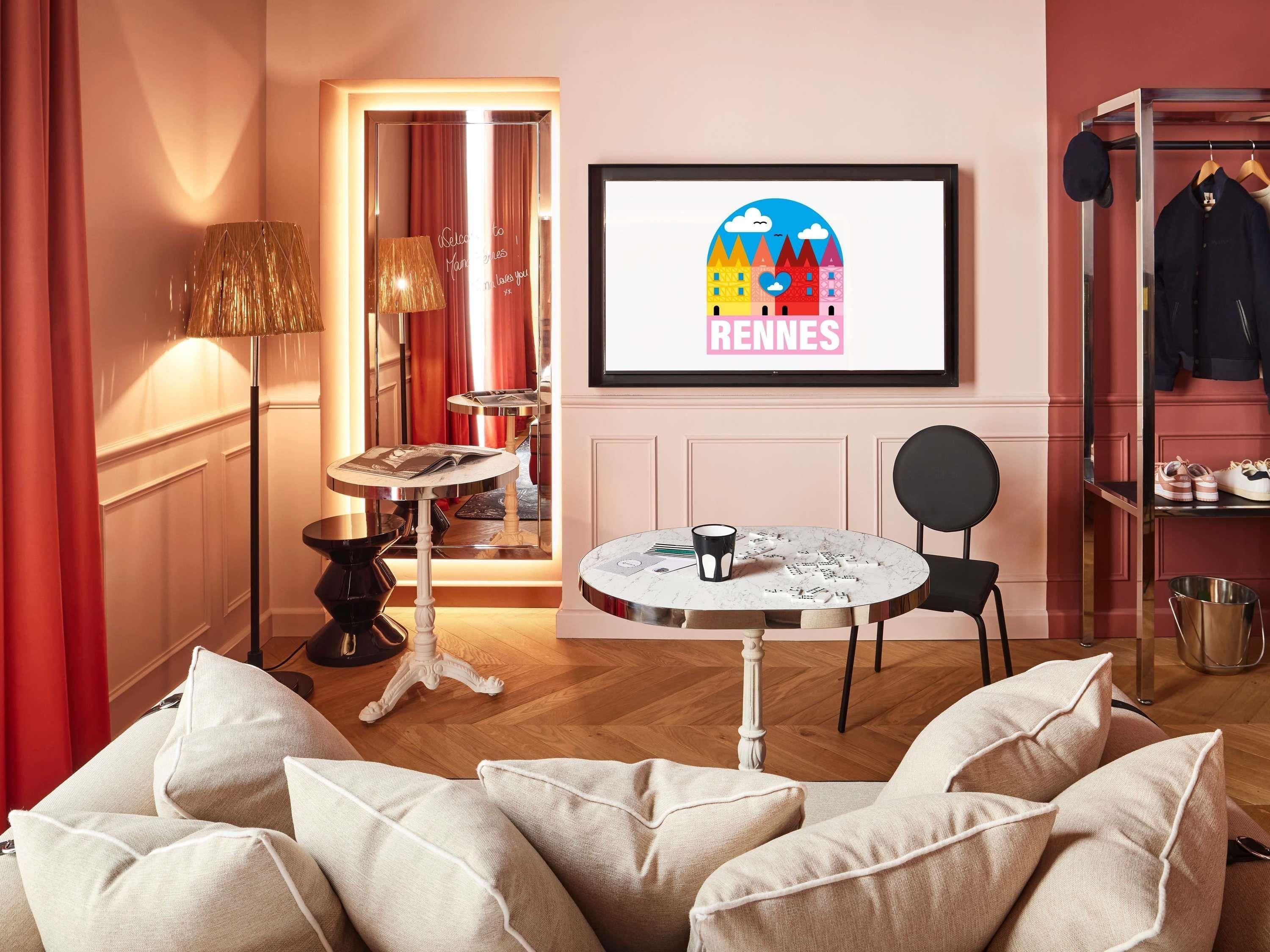 A cozy hotel room with a seating area, a framed picture of a cityscape, a small table with a cup, and a shoe rack.