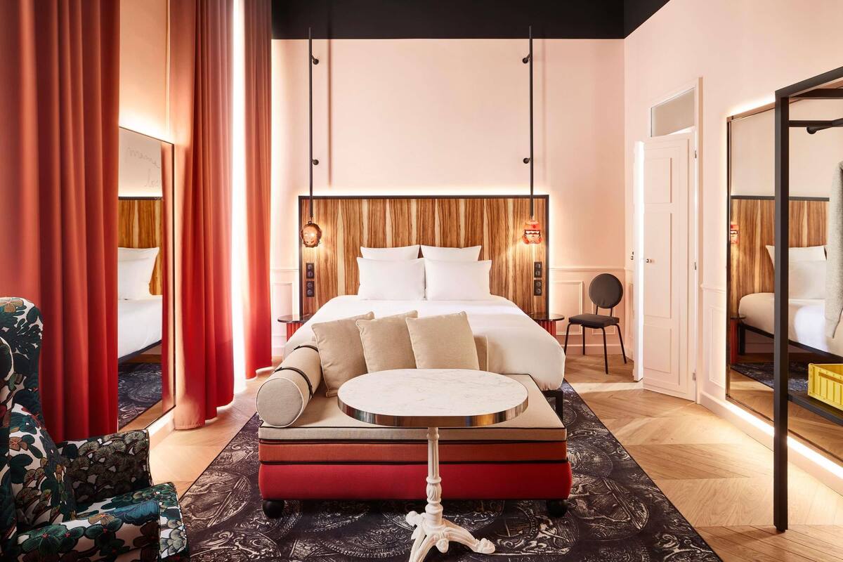 A modern hotel room with a large bed, a round side table, a chair, and a mirror.