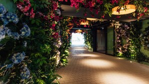 Um corredor com piso de tijolos, ladeado por folhagem exuberante e flores vibrantes.