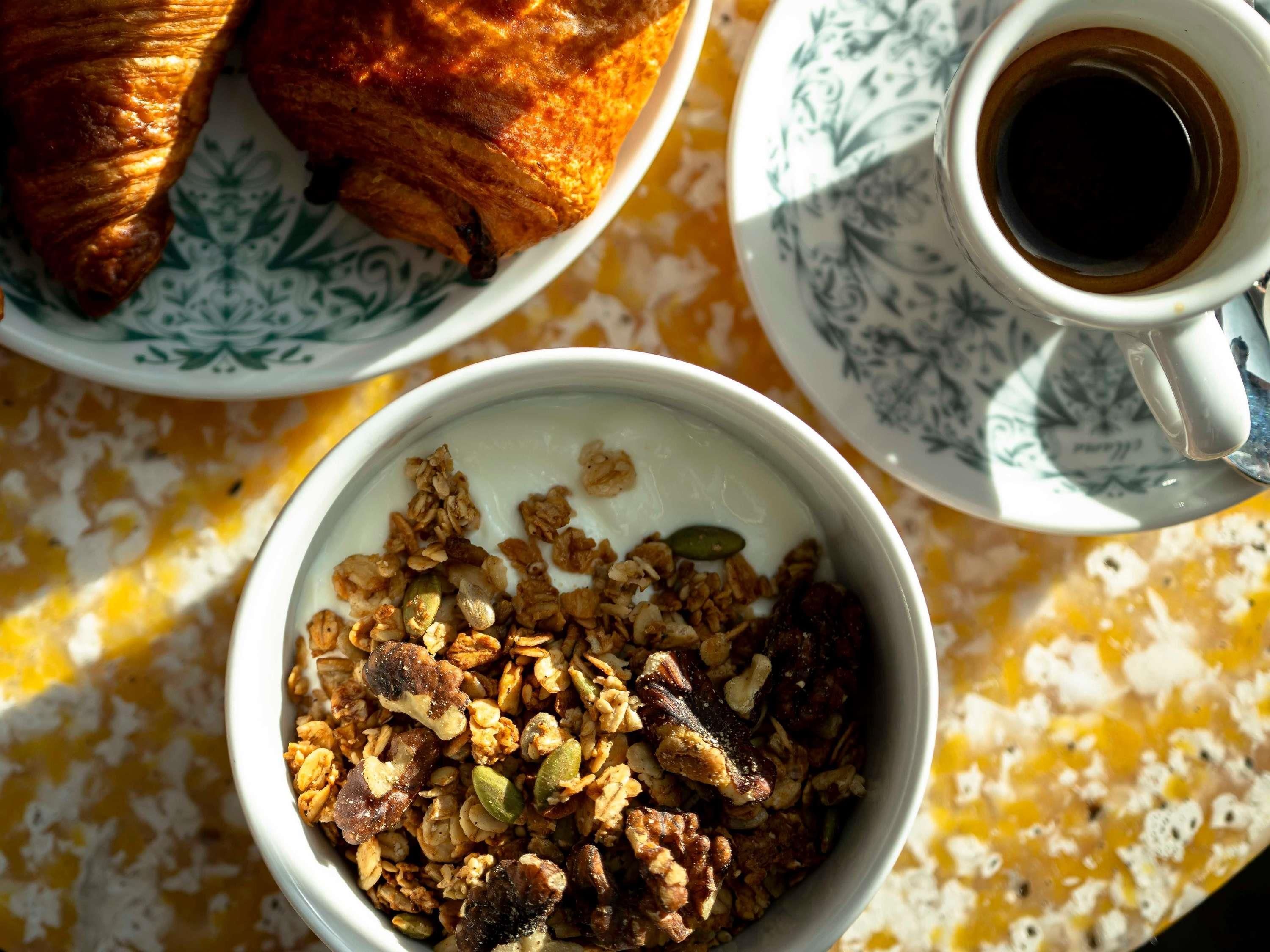 Un desayuno con un croissant, una taza de café y un tazón de granola.