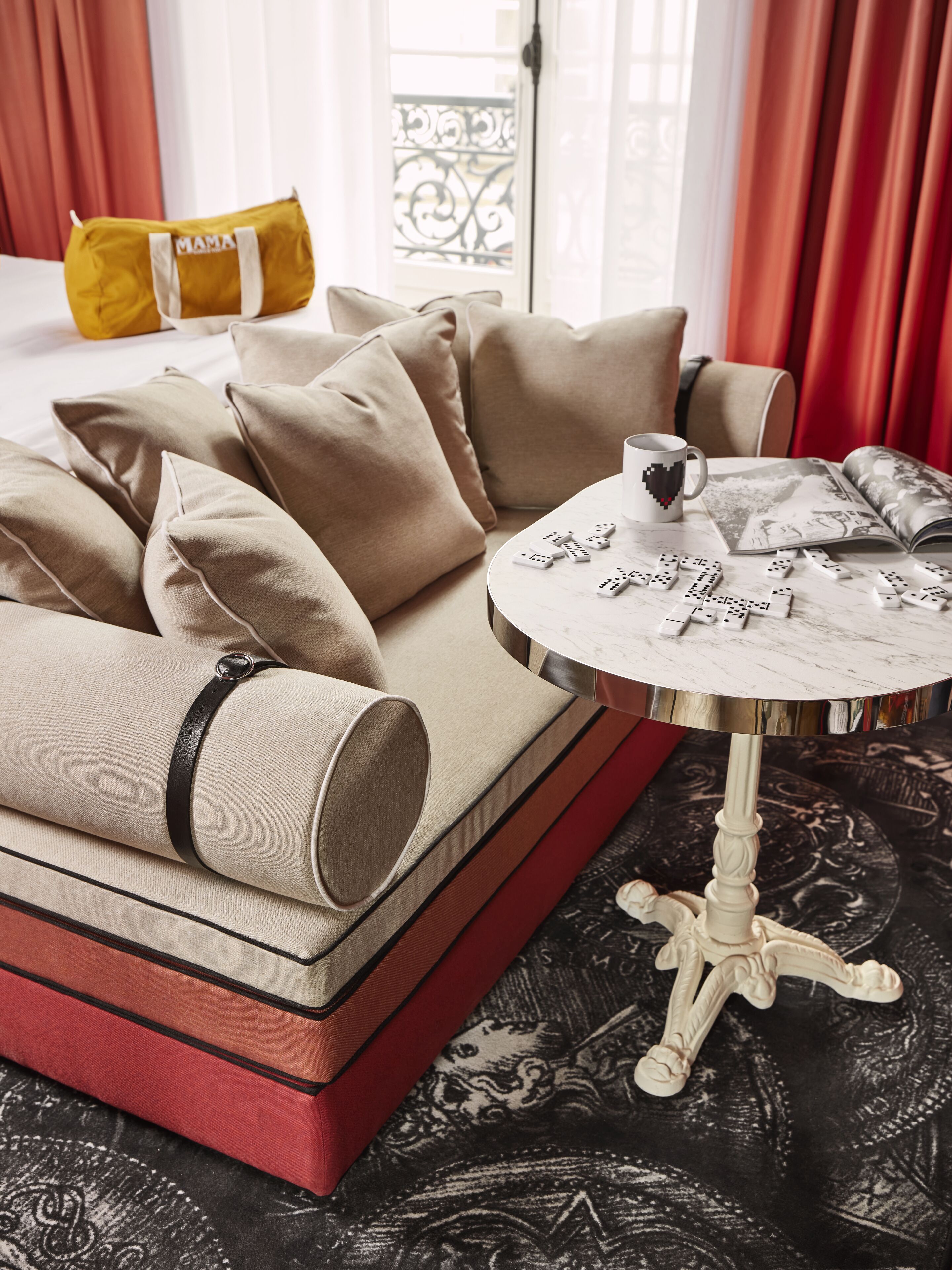 A sofa with multiple cushions, a small table with a cup and dominoes, and a patterned rug.