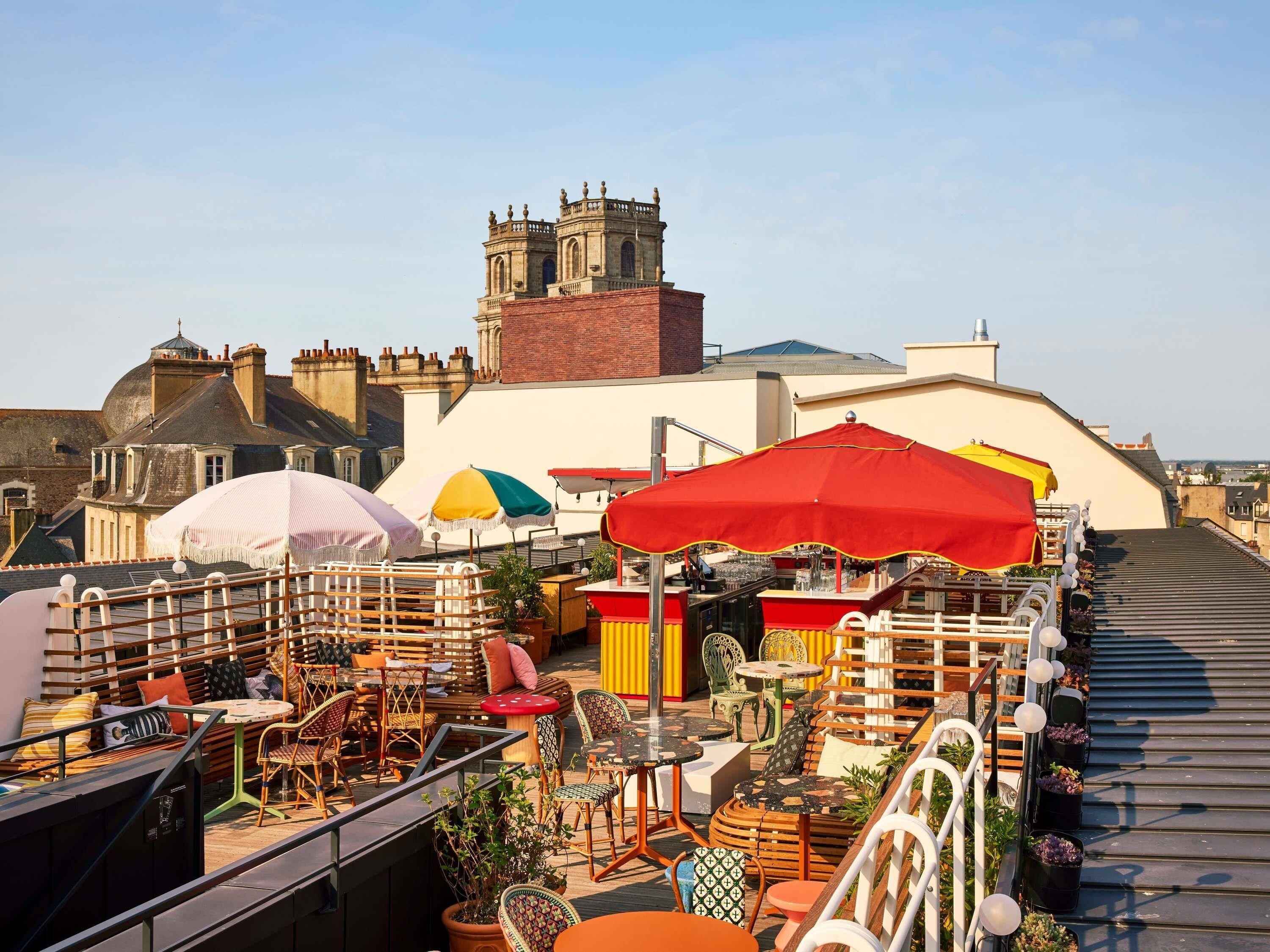 A rooftop terrace with outdoor seating, umbrellas, and a view of historic buildings.
