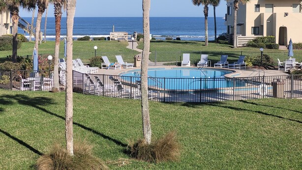 A pool area with lounge chairs, palm trees, and a view of the ocean. - Beautiful Oceanview Townhouse 2 Bed 2.5 Bath SH 430 (St. Augustine)