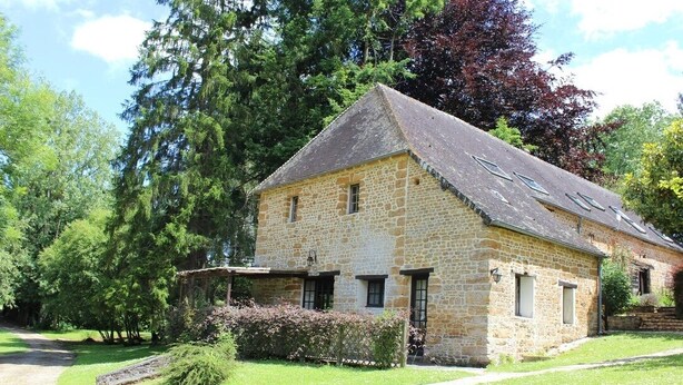 Ein Steinhaus mit geneigtem Dach, einer kleinen Veranda und einem gepflegten Rasen.