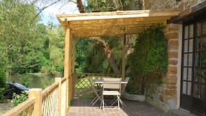 Eine Holzterrasse mit Tisch und Stühlen, eine Steinmauer und Blick auf einen Fluss.
