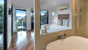 Ein modernes Hotelzimmer mit einem großen Bett, einer Badewanne und einem Balkon mit Blick.