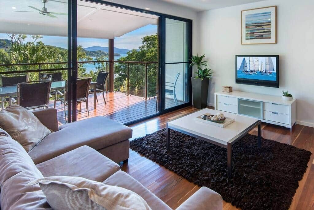 A modern living room with a sofa, coffee table, TV, and a balcony with a view of the outdoors.