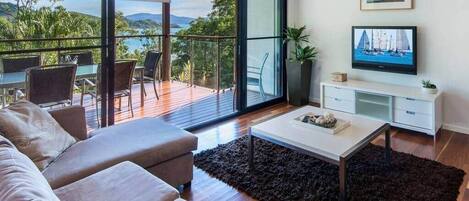 A modern living room with a sofa, coffee table, TV, and a balcony with a view of the outdoors.