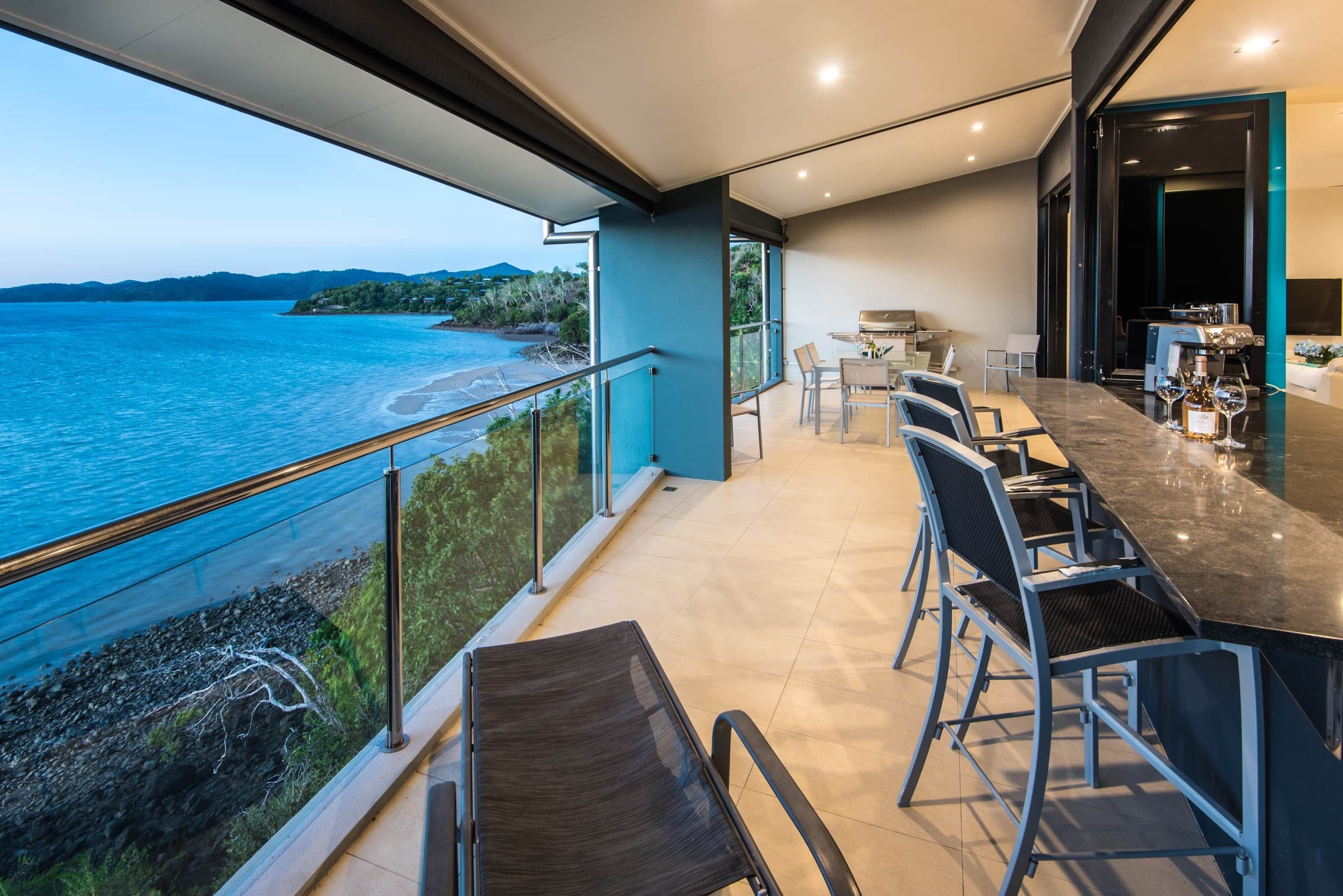 A modern outdoor dining area with a view of the sea and hills.
