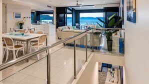 A modern, multi-level living space with a dining area, kitchen, and seating area with a view of the sea.