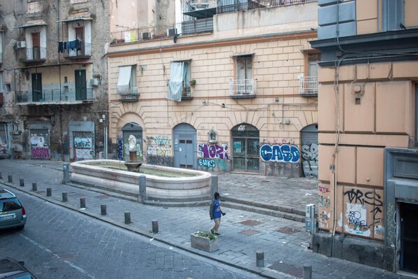 Une rue bordée d’immeubles, avec une fontaine et une personne qui marche.