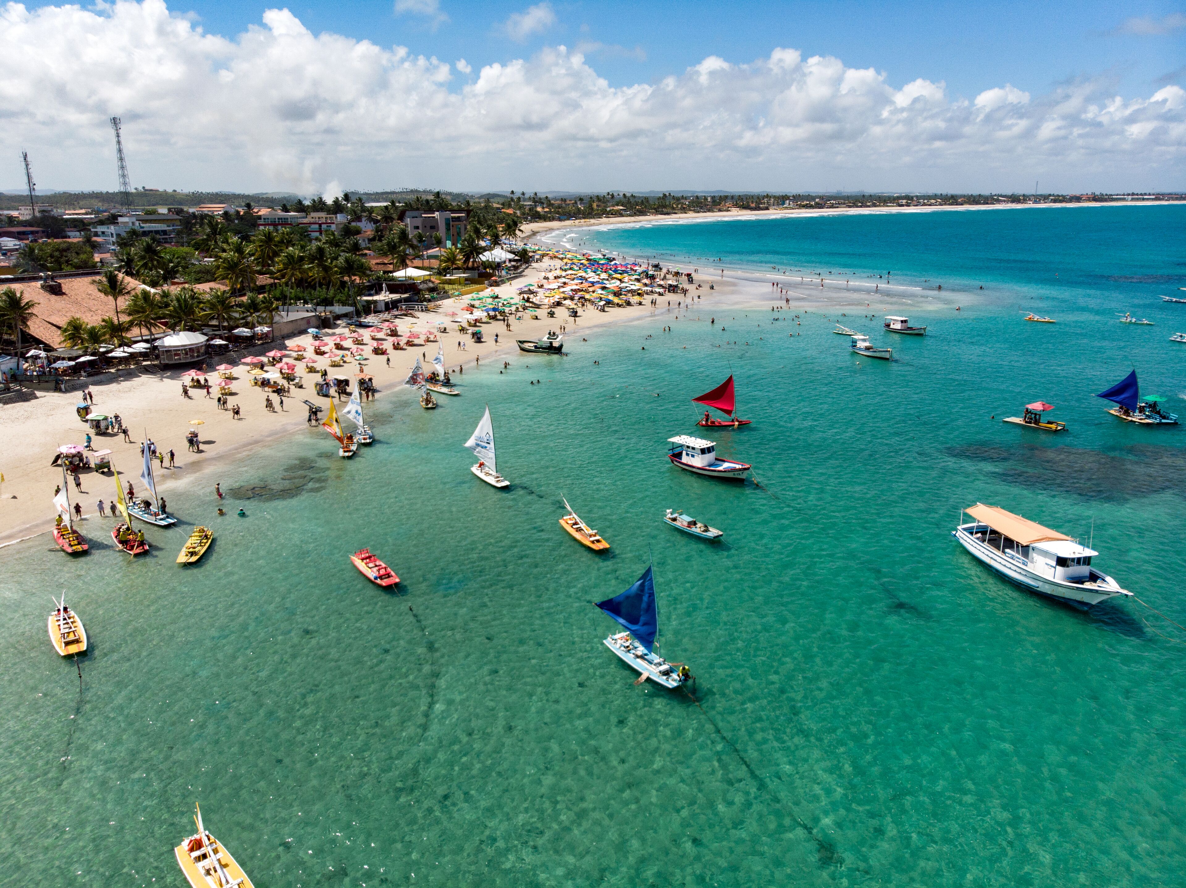 Une plage à l’eau turquoise et limpide, où l’on peut voir de nombreux bateaux et des parasols.