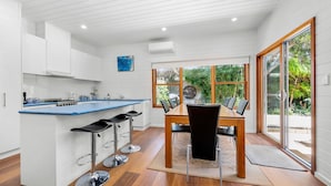 A modern kitchen with a blue countertop, white cabinets, and a dining area with a wooden table and black chairs. - Esplanade Premium 33 Steps to Beach (Torquay)