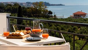 Un tavolo da balcone con prodotti per la colazione, vista sul mare e un vigneto sullo sfondo.