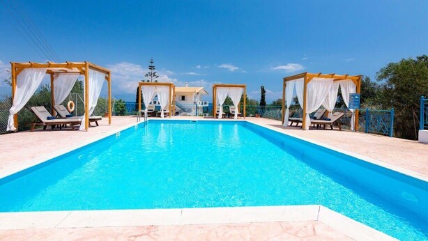 Piscina con quattro lettini prendisole e tende da sole, circondata da una recinzione e alberi.