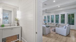 A modern interior with a white paneled wall, a built-in kitchen with a sink and cabinets, and a living area with a sofa and a coffee table. - Clubhouse Amenities and 6-Seat LSV (Santa Rosa Beach)