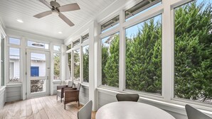 A sunroom with large windows, wicker chairs, a round table, and a ceiling fan. - Clubhouse Amenities and 6-Seat LSV (Santa Rosa Beach)