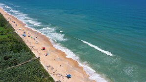 Vista aérea de uma praia com fileiras de guarda-sóis e cadeiras de praia ao longo da orla.