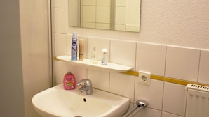 Un bany amb un lavabo blanc, un mirall i prestatges amb productes de tocador.