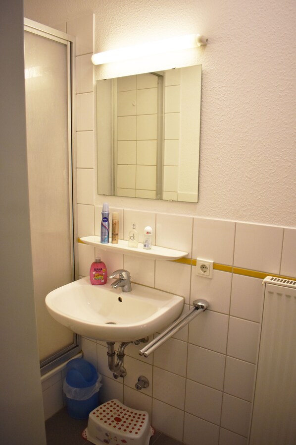A bathroom with a white sink, mirror, and shelves with toiletries.