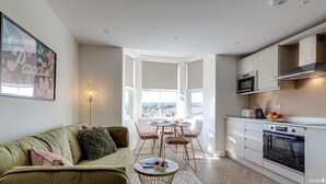 A modern kitchen with white cabinets, a microwave, and an oven. There is a dining area with a table and chairs, and a large window offering a city view. - North Marine Villa - Apt 3 - Second floor modern apartment near North Bay Beach. (Scarborough)