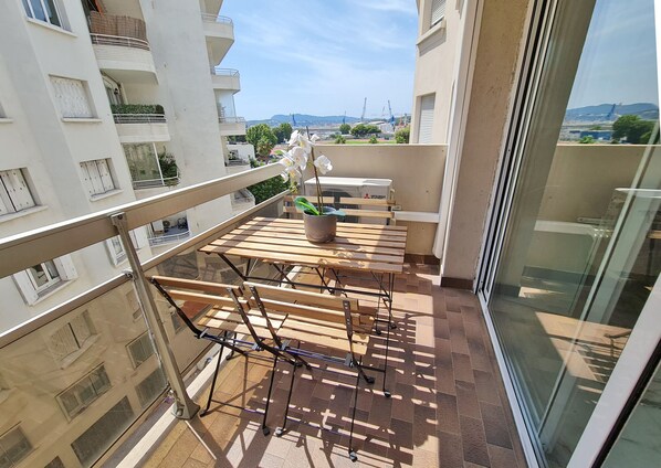 A balcony with a wooden table and chairs, a potted plant, and a view of the cityscape.