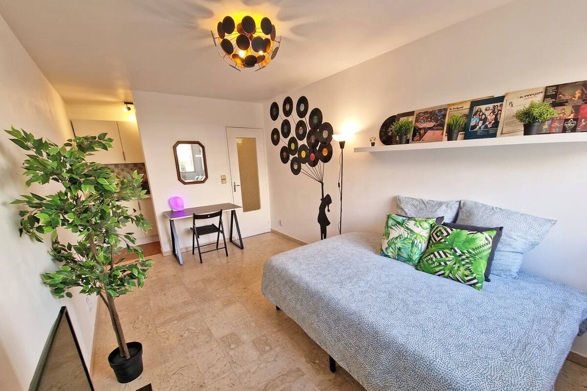 A bedroom with a bed, a desk, a chair, a mirror, a wall with vinyl records, and a ceiling light fixture.