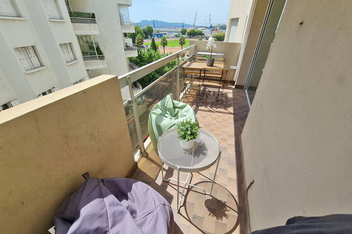 A balcony with a small table and chairs, a green bean bag, and a potted plant.
