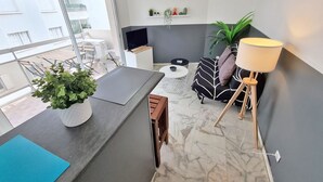 Una sala moderna con piso de mármol, un sofá con cojines estampados, una mesita redonda pequeña, un televisor sobre un mueble y una planta en maceta.