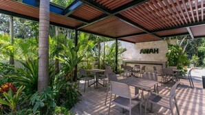 An outdoor patio with tables and chairs, surrounded by lush greenery and a stone wall with the name "ANAH" visible. - 2BR Condo Beautiful Common Areas, Sleeps 6! (Akumal)